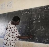 A teacher in South Sudan writes a math problem on the blackboard.