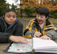 Two boys look at a book of picture symbols together.