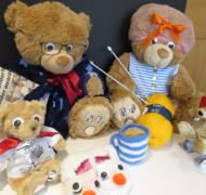 a group of stuffed bears with a knit tea cup and treats in front of them