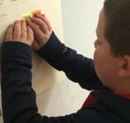 A boy reads his braille calendar on the wall.