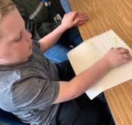 A boy checks his work on a braille assignment.