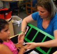 A young girl examines a tactile calendar with her teacher