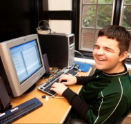 A teenage boy writes on a desktop computer