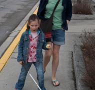 A young girl walks with a white cane