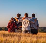 teens from behind with their arms around each other in an open field