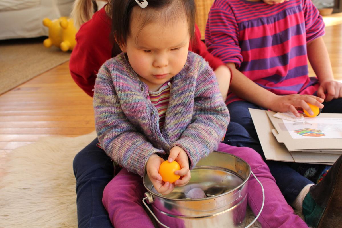 A girl playing with tactile items in a metal bucket