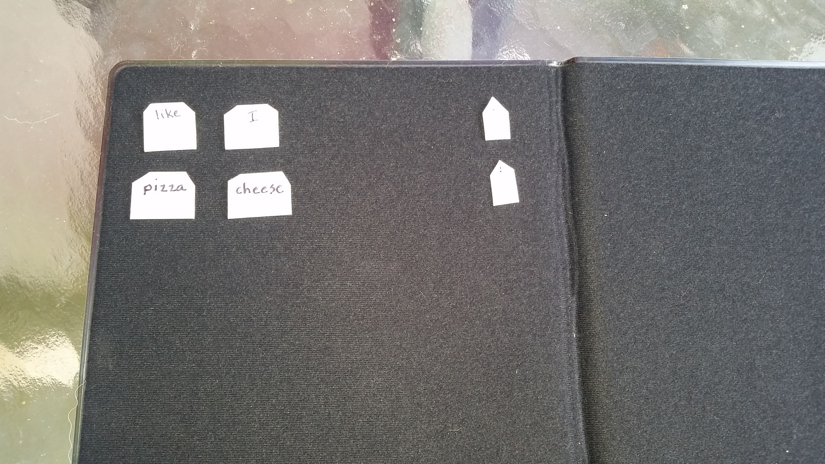 The braille words I, cheese, pizza, and like and a period are on small plastic tiles on a black felt board from APH.