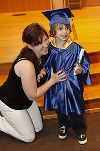 A woman kneels next to a child in a cap and gown