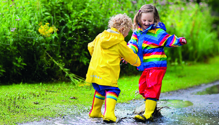 Children wearing rubber boots splashing in a puddle