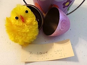 yellow chick next to open purple plastic egg with a note in braille "I love you"