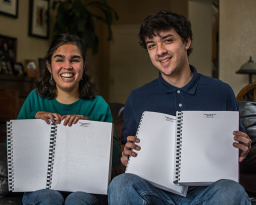 A student holds up her braille year book next to her twin brother