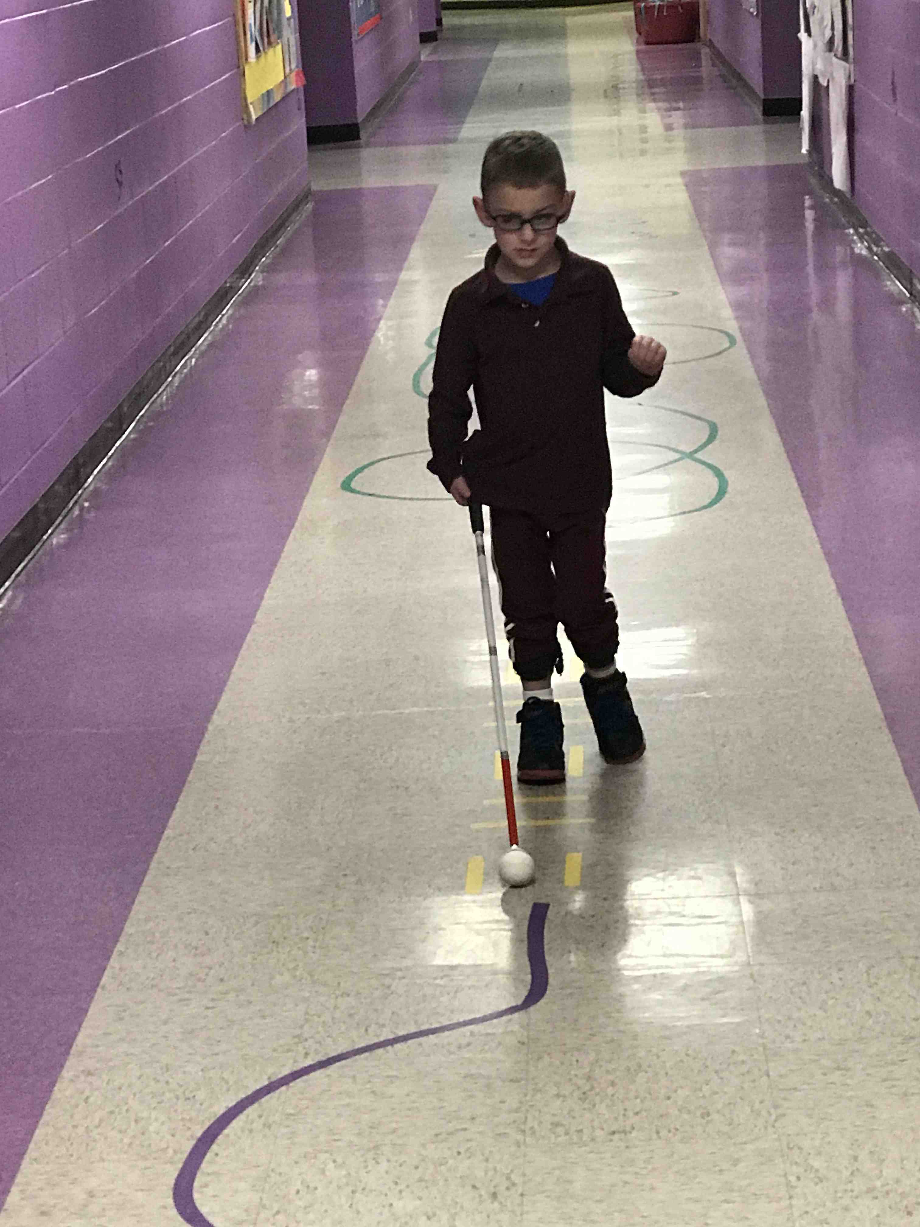A young boy walks in a school corridor using his cane