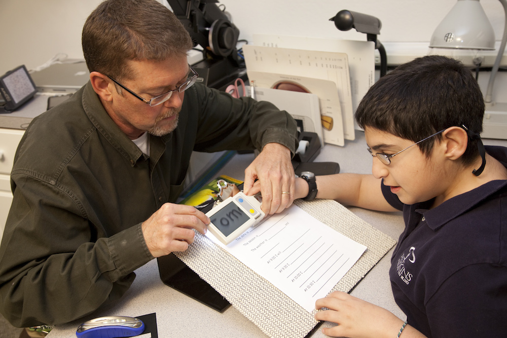 boy and teacher using magnifying screen to read