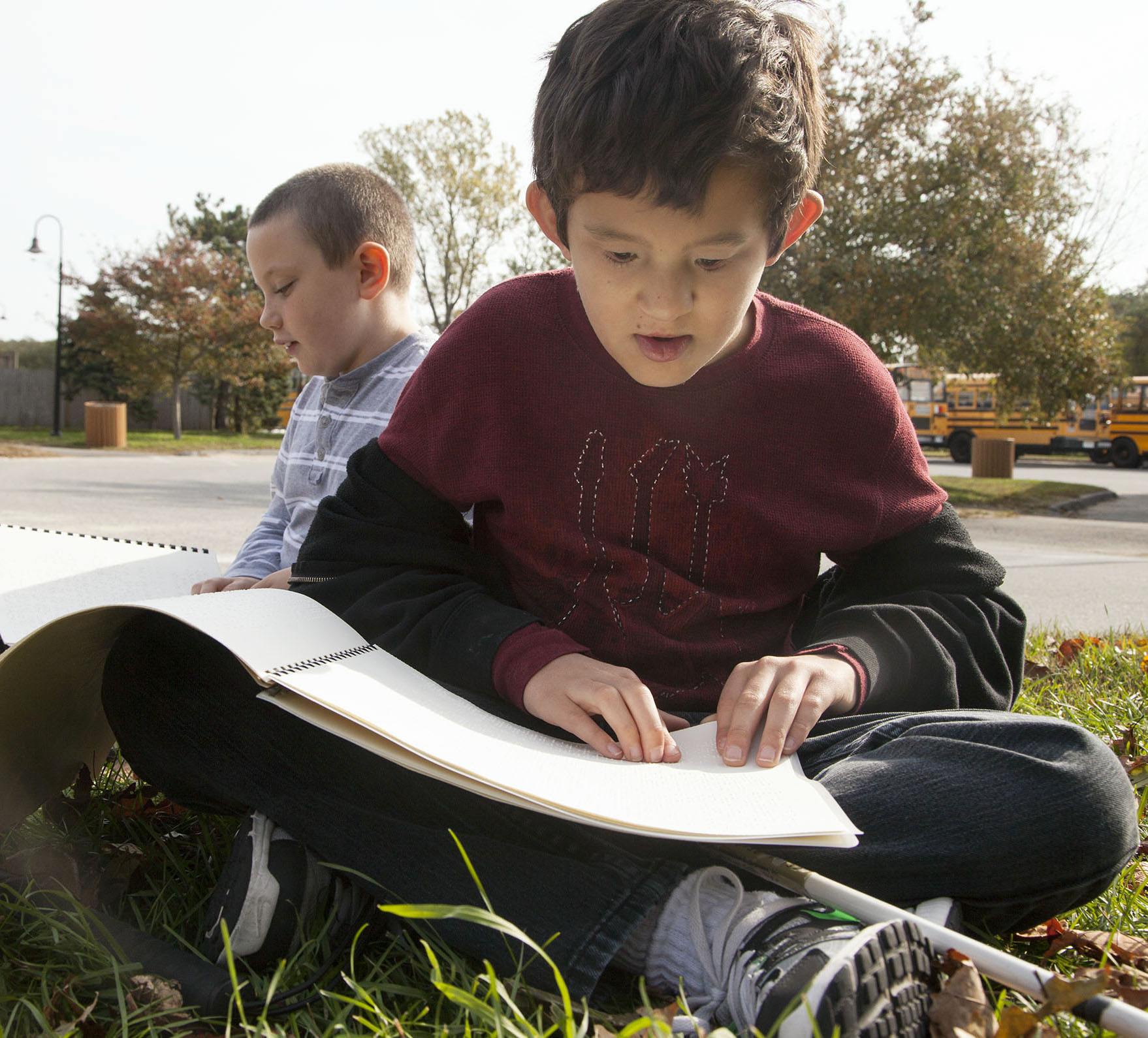 two boys read braille books outside