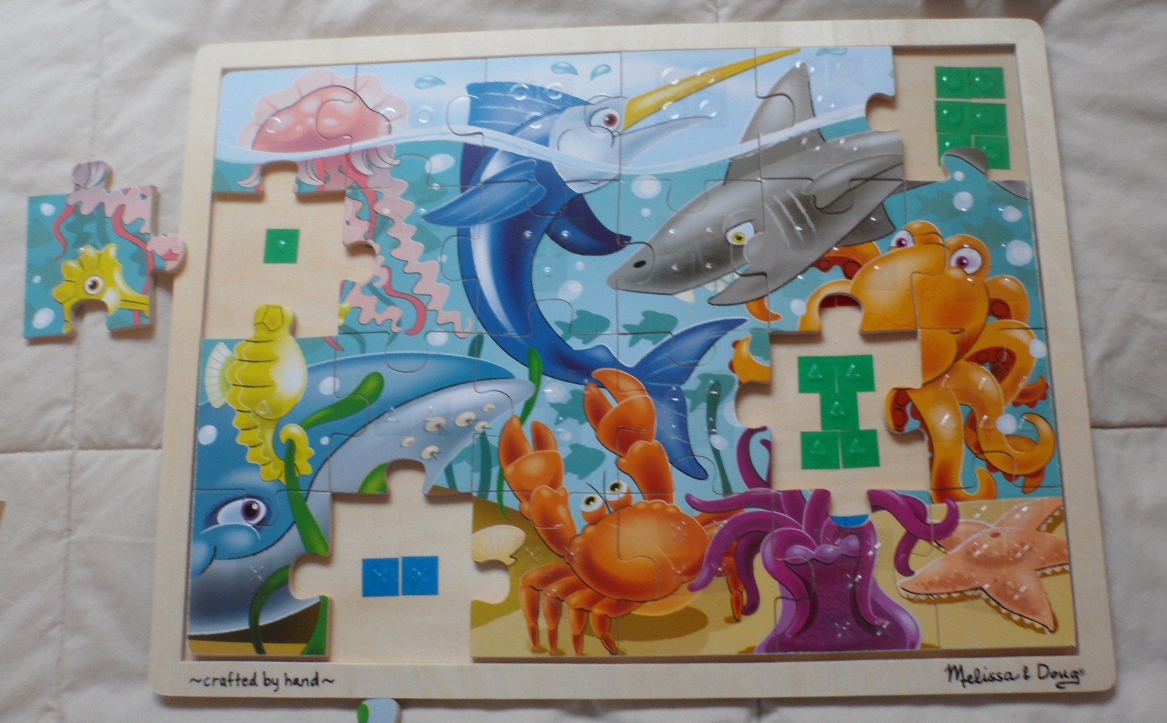 Jigsaw puzzle near completion, shows placement of tactile stickers on the frame underneath each piece.  Transparent tactile symbols on jigsaw picture are faintly visible.