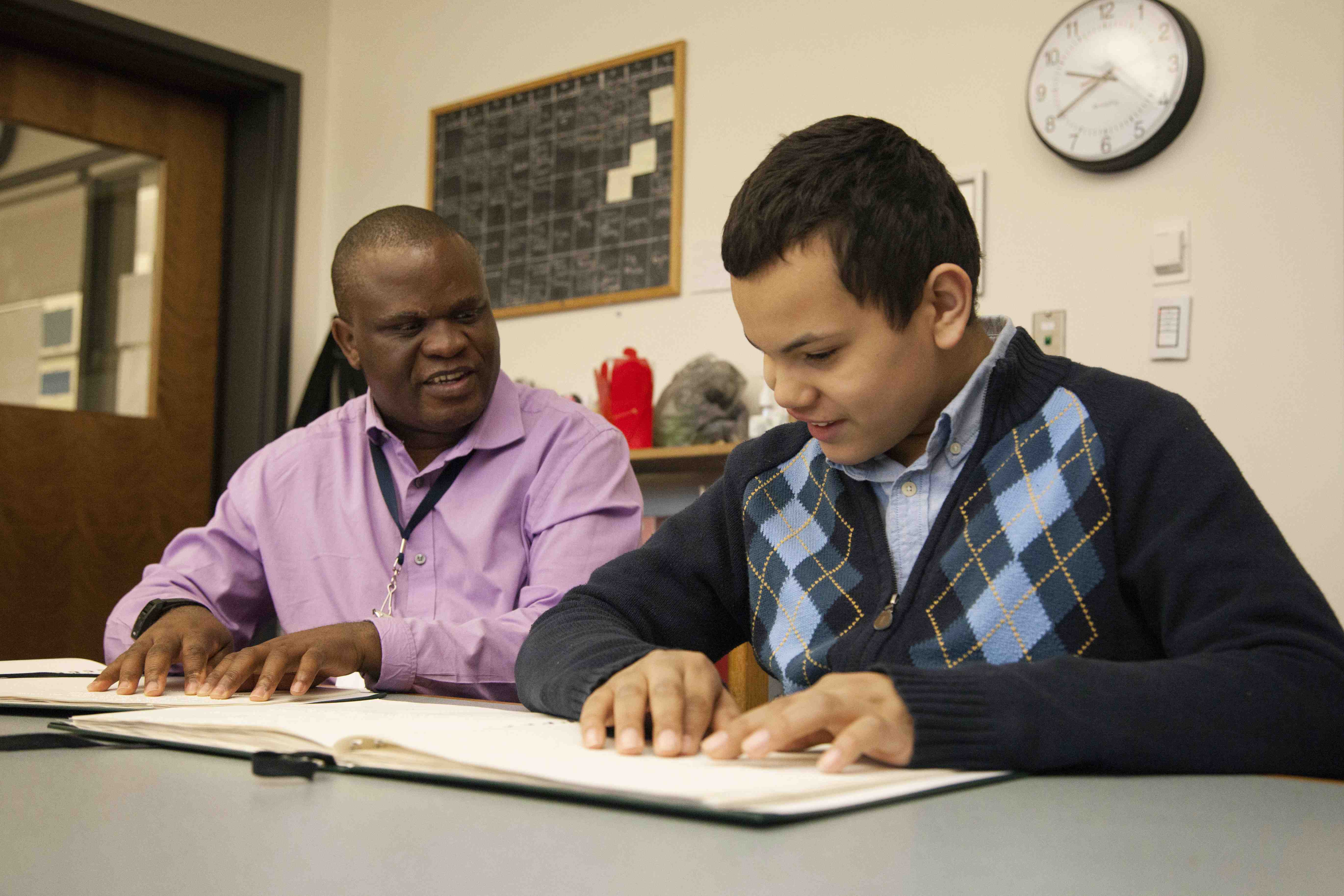 A teacher and student read braille together