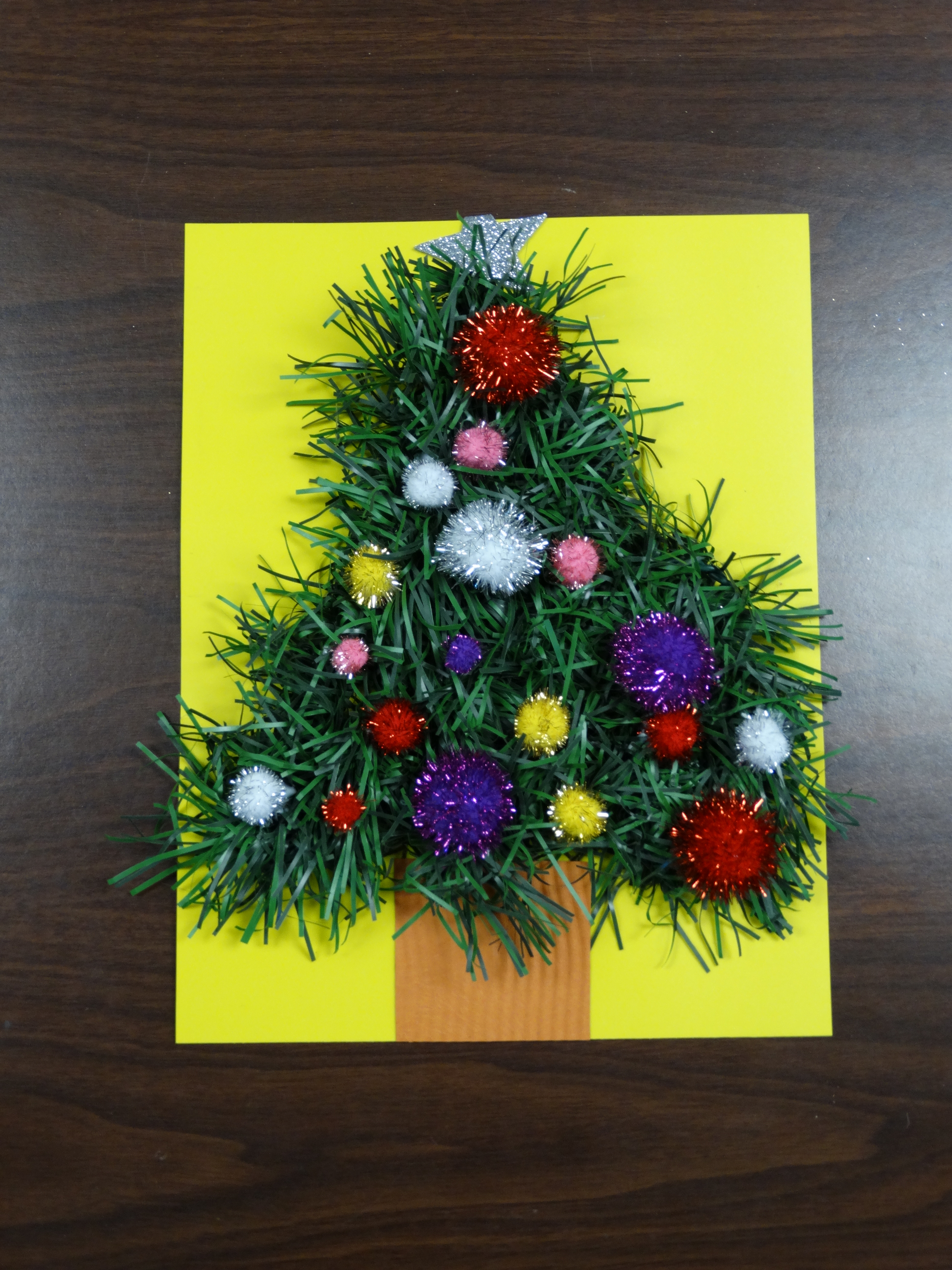 garland shaped into a tree with fuzzy pom poms on a piece of yellow paper