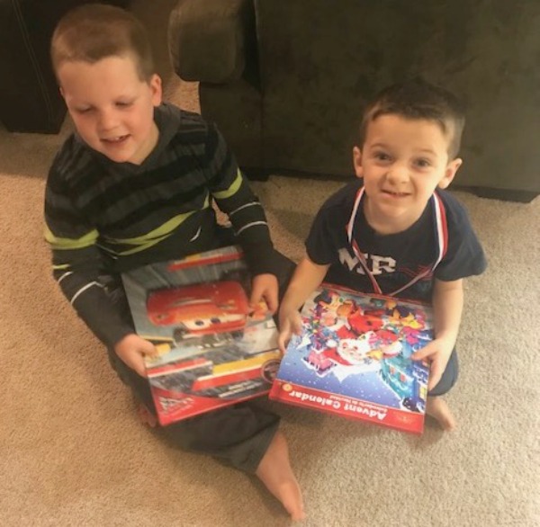 Two boys sitting on rug holding their calendars