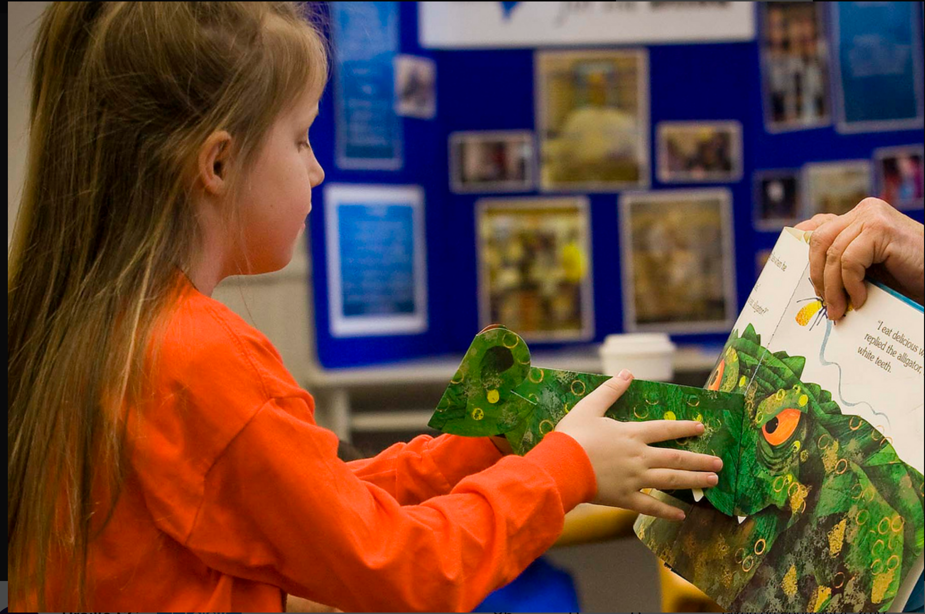 A young girl examines a pop-up illustration of an alligator nose in a picture book