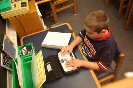 A boy uses a Braille Note at his desk.