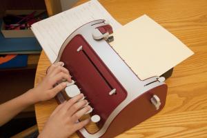 Student writing on a braille writer