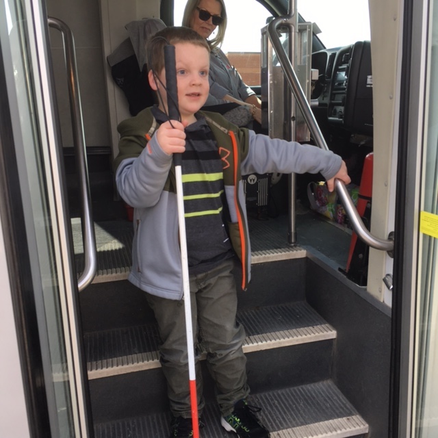 A young boy steps down out of a bus while holding his cane