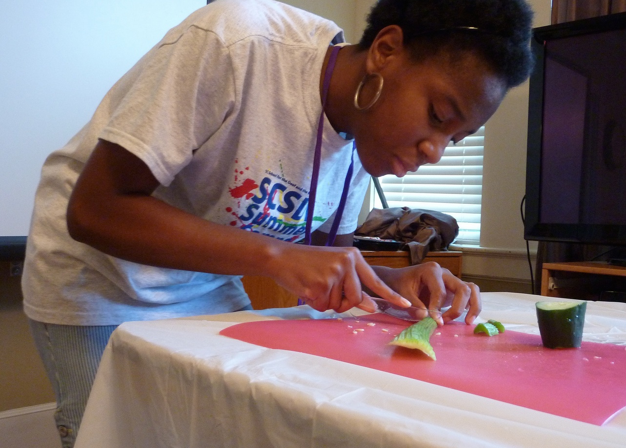 A young woman cuts celery on a red cutting board.