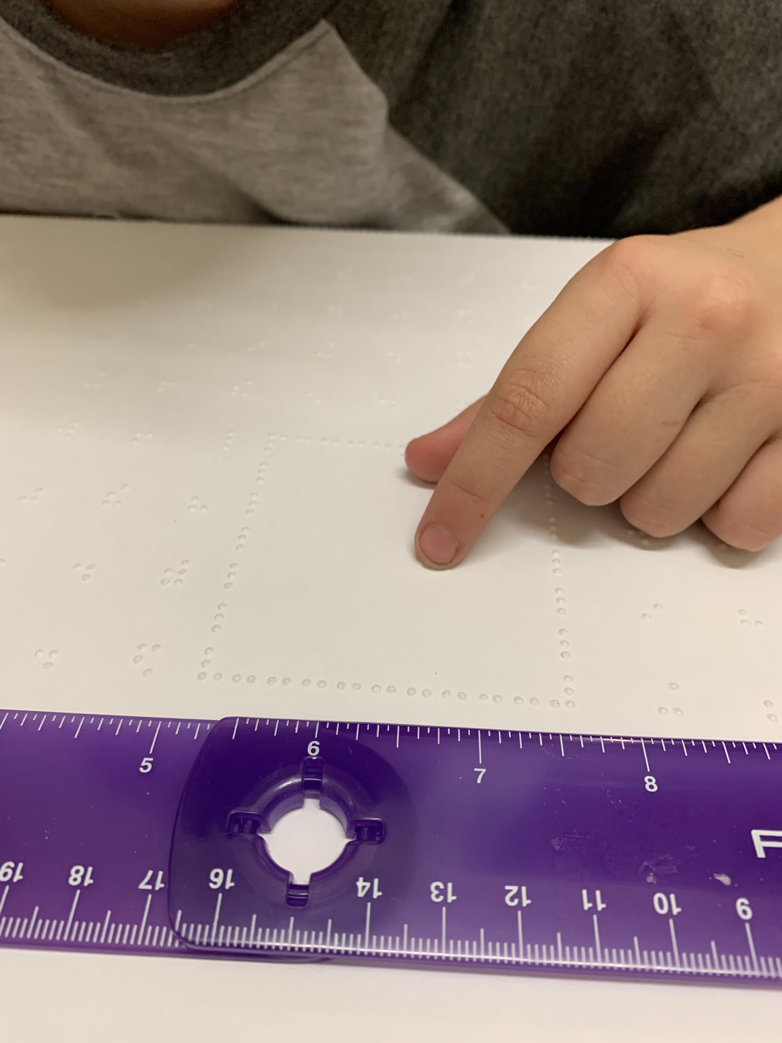 Hand on paper with braille with purple ruler at top of paper