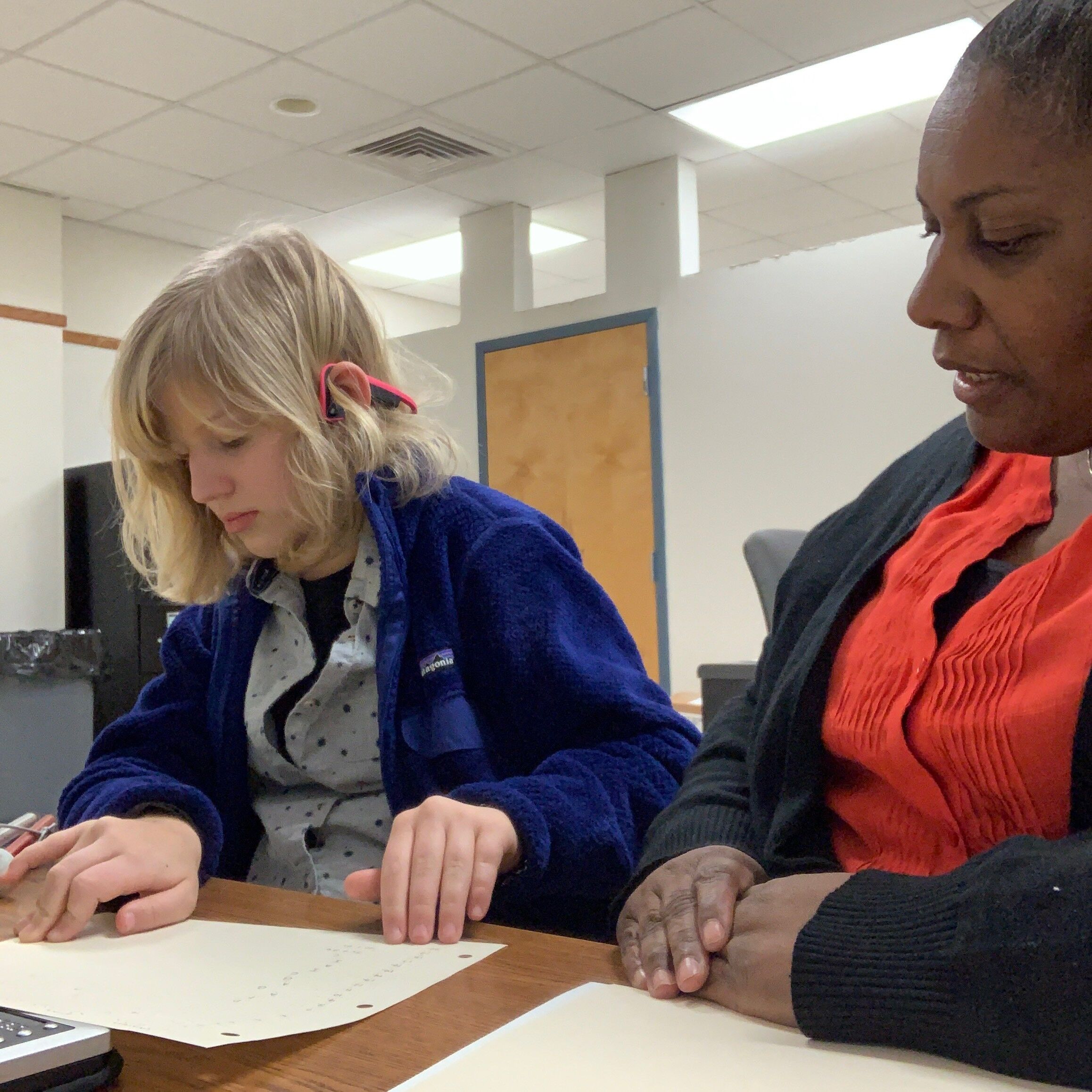 A girl reads braille next to her paraprofessional