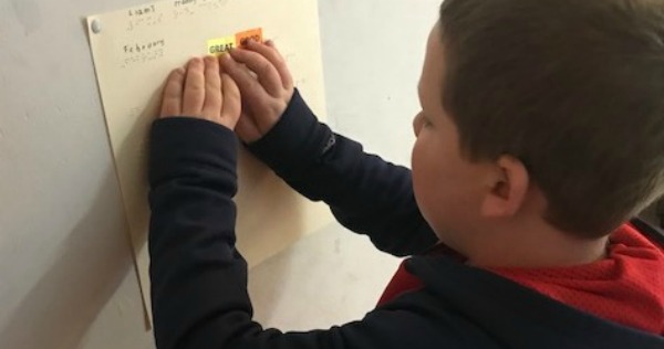 A boy reads his braille calendar on the wall.