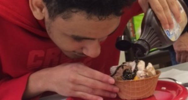 A boy puts chocolate syrup on his ice cream.