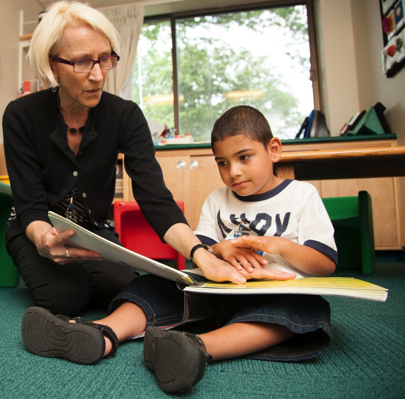 Teacher reading braille book with young boy