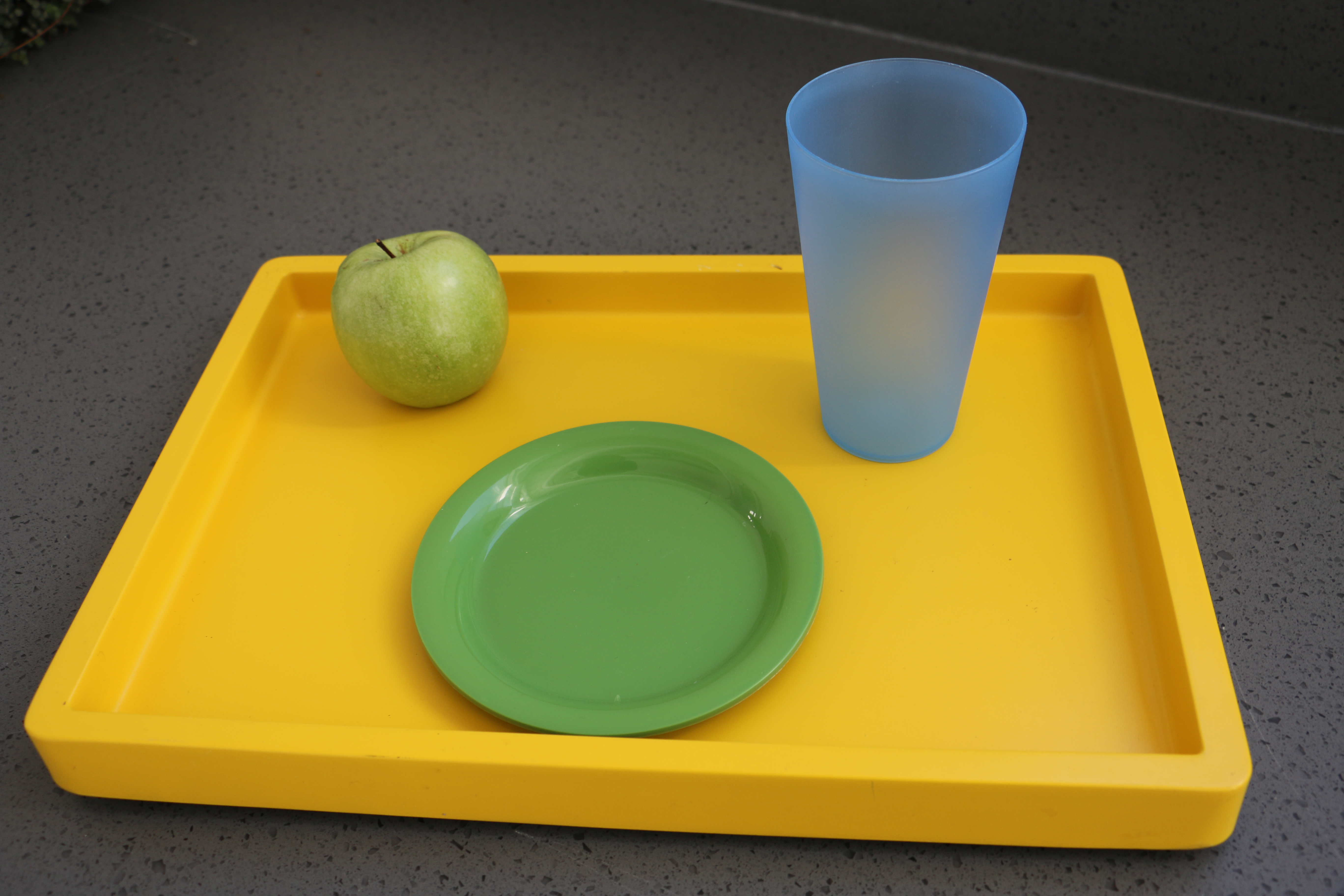 yellow tray with green plate, an apple and a blue cup