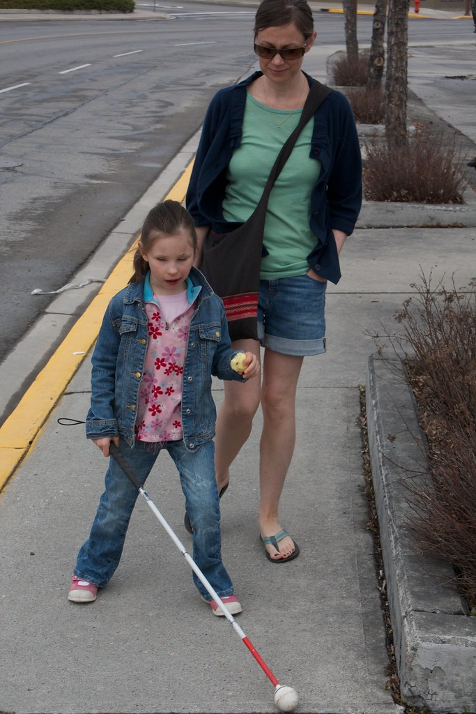 A young girl walks with a white cane